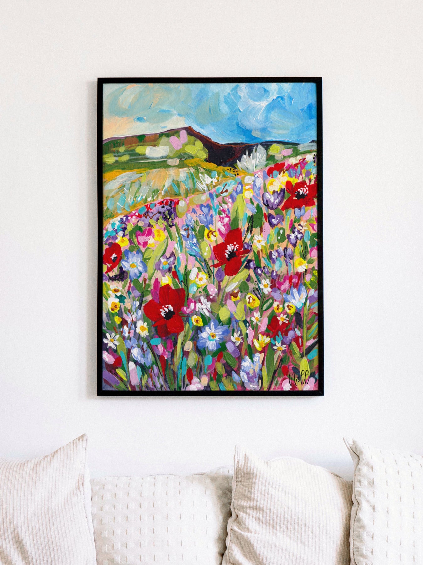 Framed painting of a colorful floral landscape on a white wall above a sofa.