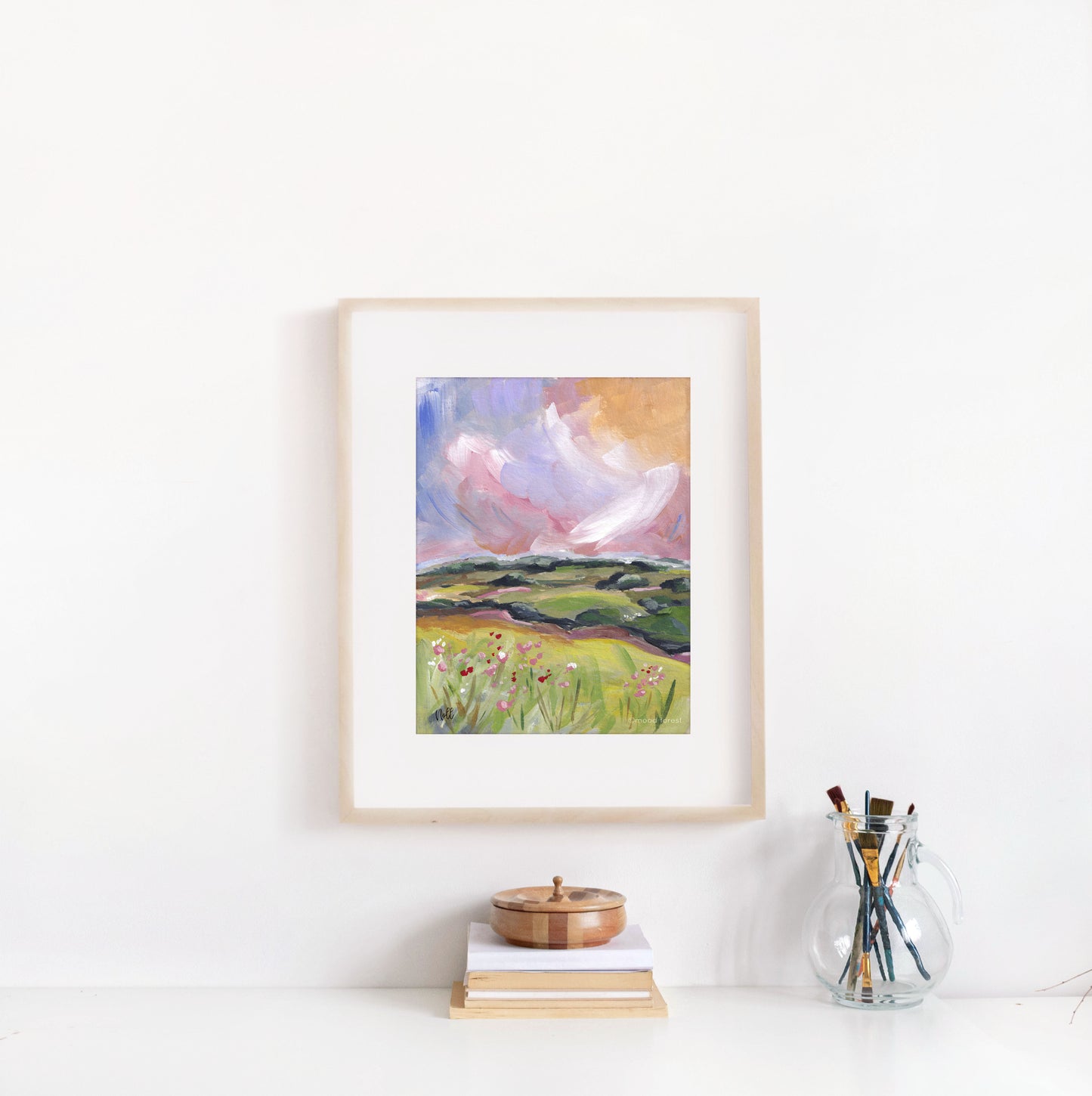 Framed painting of a landscape with a pink sky on a white wall.