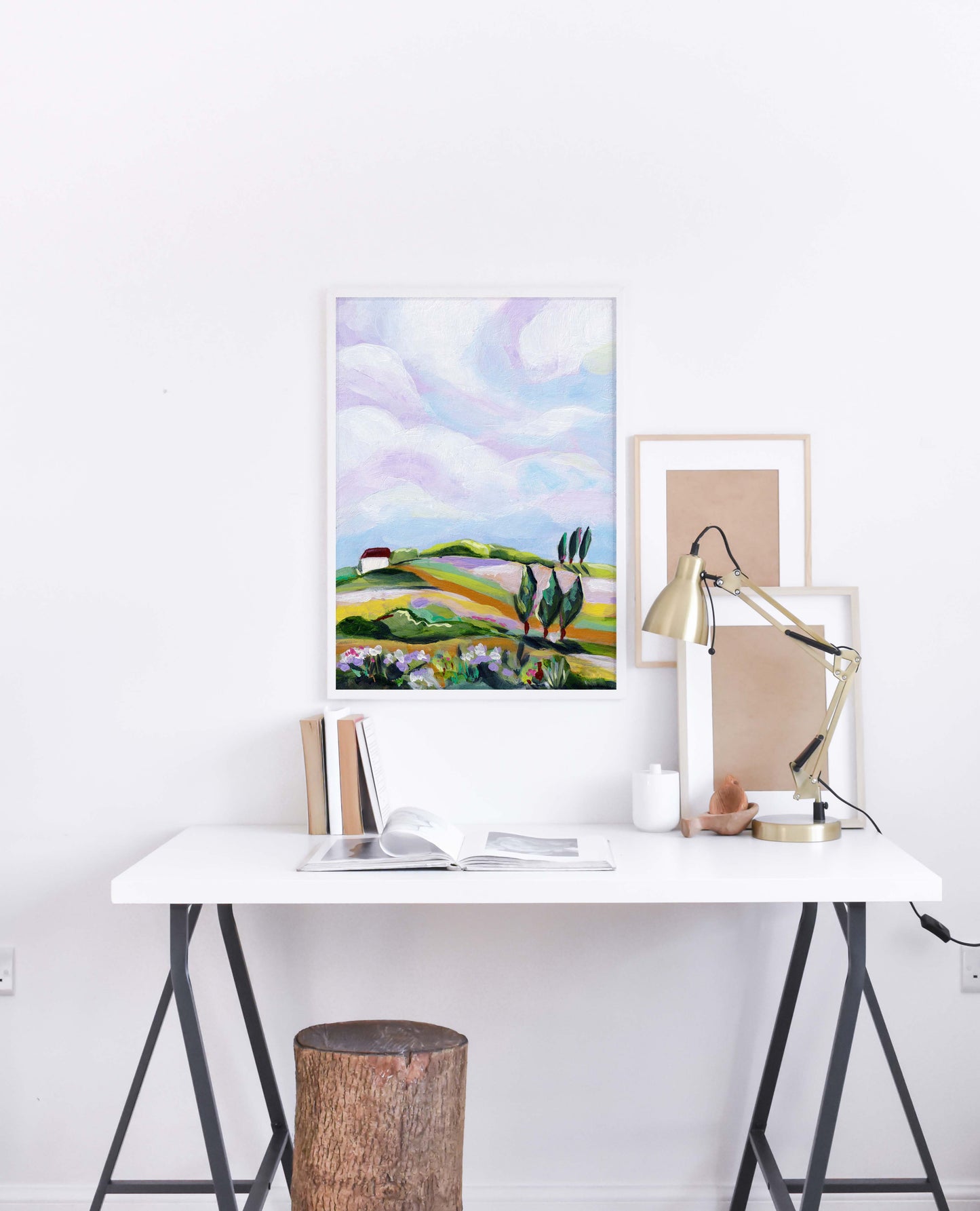 Modern office setup with a desk, lamp, and framed artwork on a white wall.