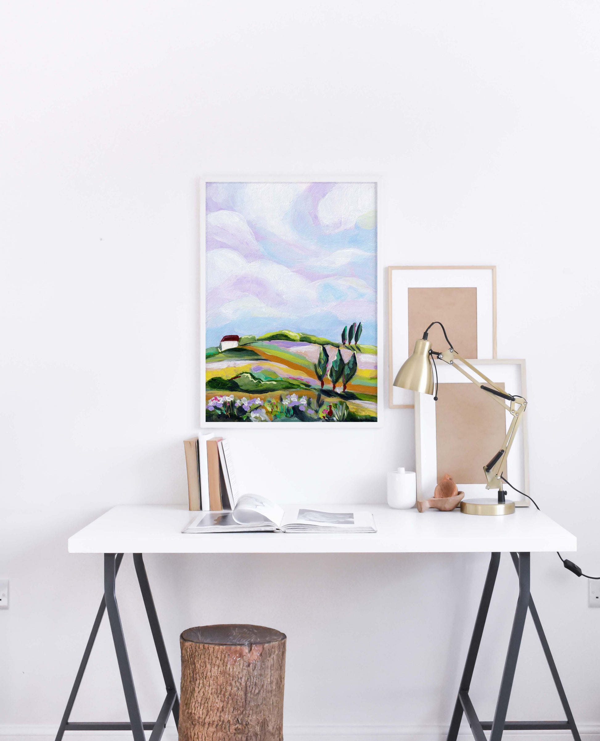 Modern office setup with a desk, lamp, and framed artwork on a white wall.