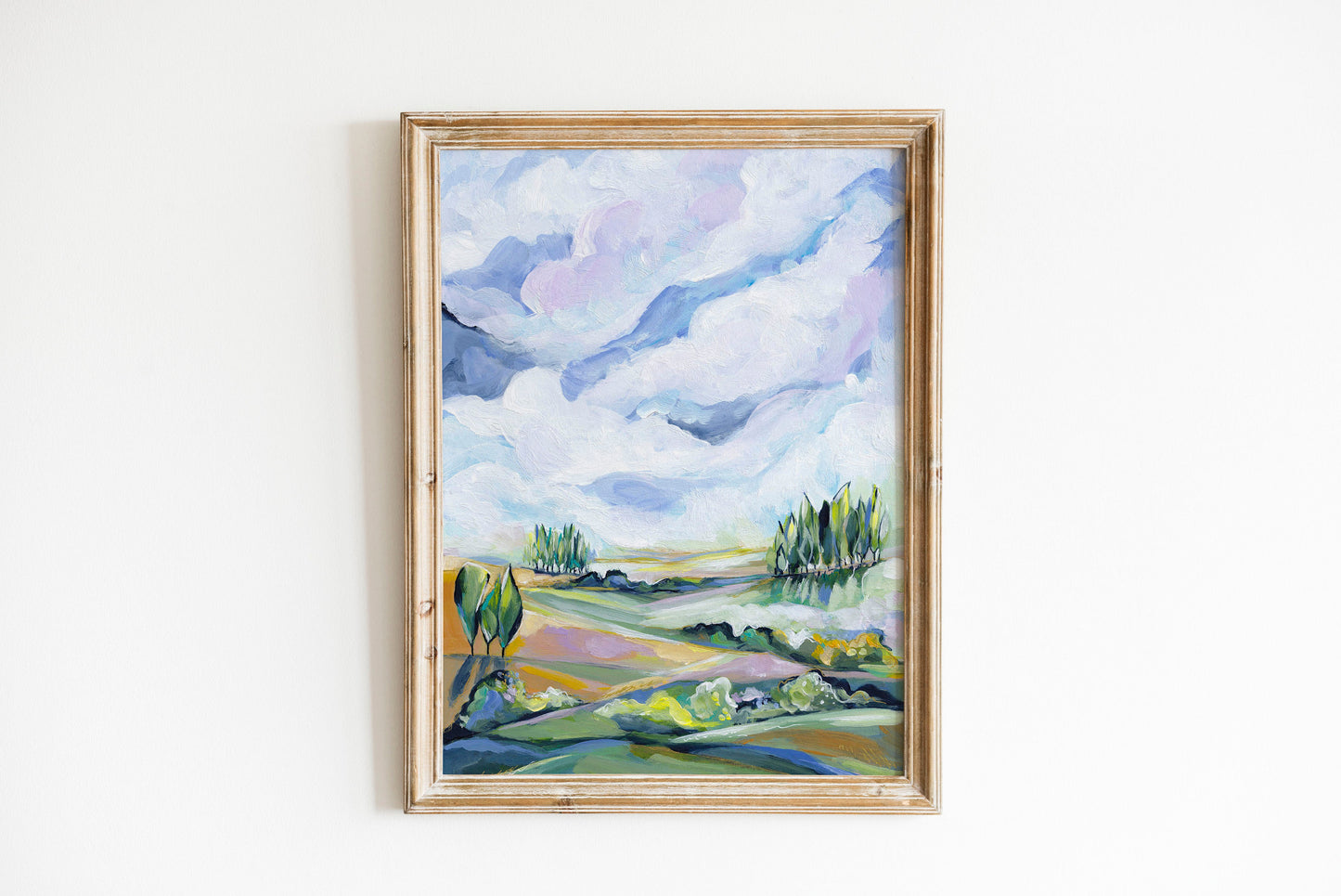 Framed painting of a landscape with trees and clouds on a white wall