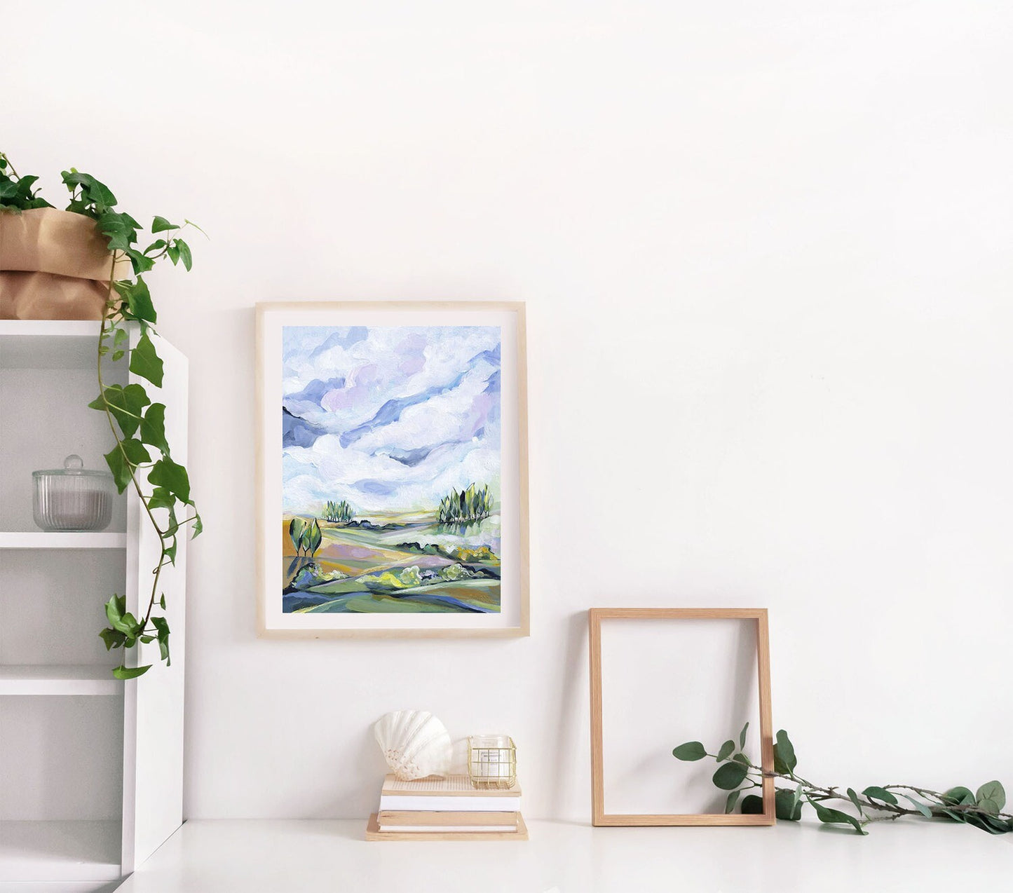Framed landscape painting on a wall with a shelf and plant in the background