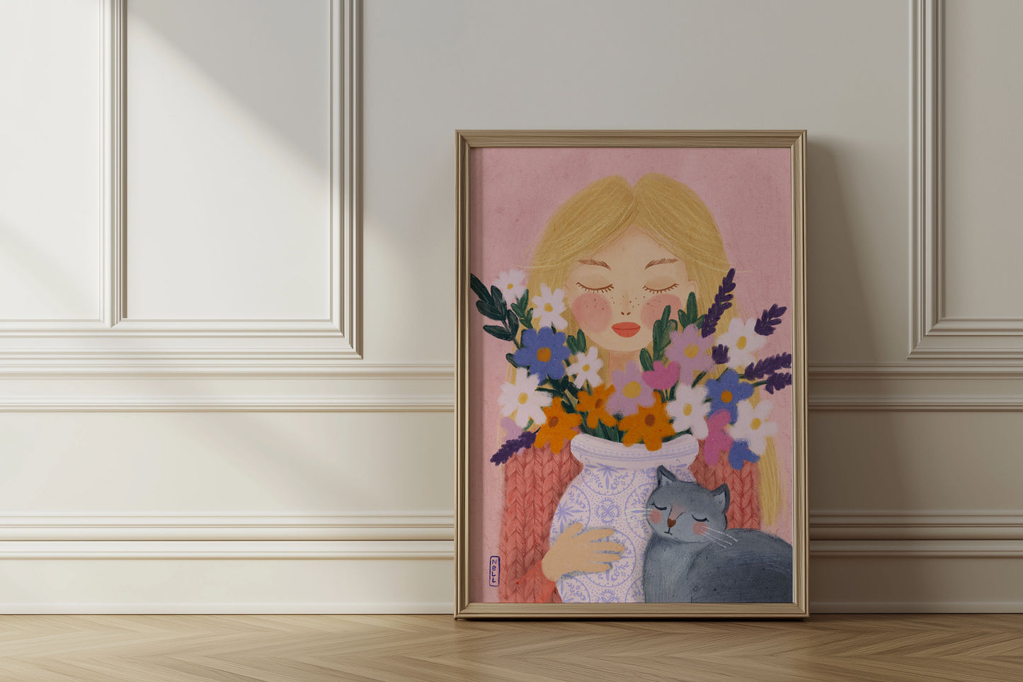 Framed artwork of a woman holding flowers and a cat against a pink background, displayed on a wall.