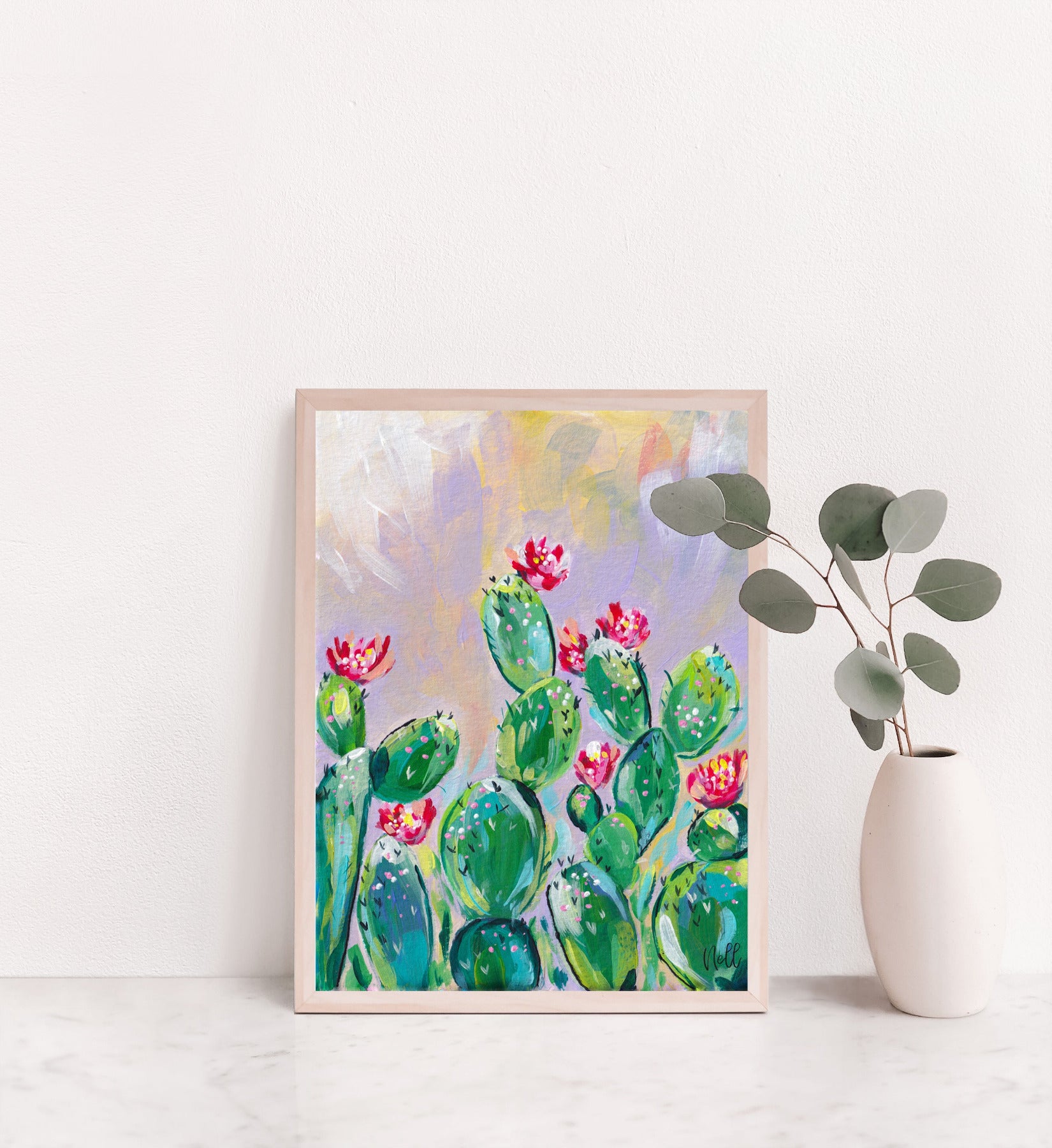 Framed artwork of cacti with pink flowers on a white wall.