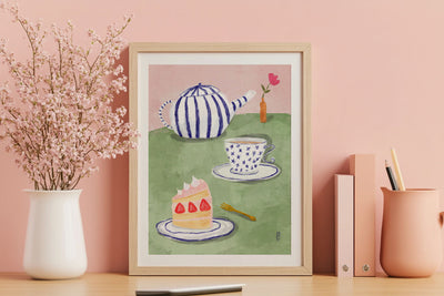 Framed artwork of a teapot, cake, and teacup on a pink wall with decorative items.