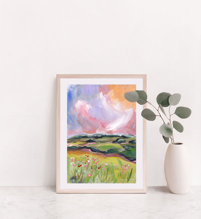 Framed artwork of a colorful landscape with flowers and a cloud, placed on a white surface.