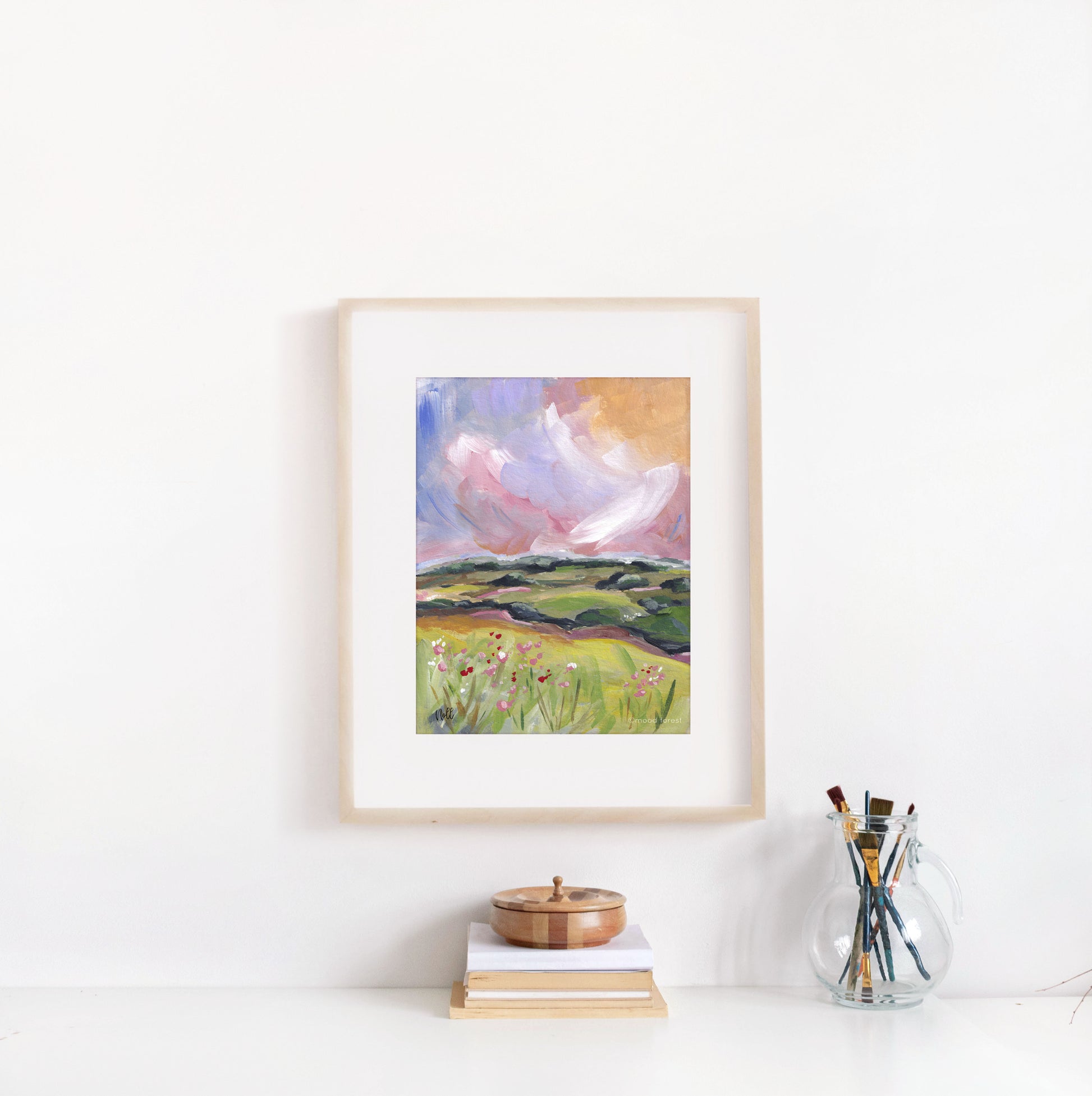 Framed painting of a landscape with a pink sky on a white wall.