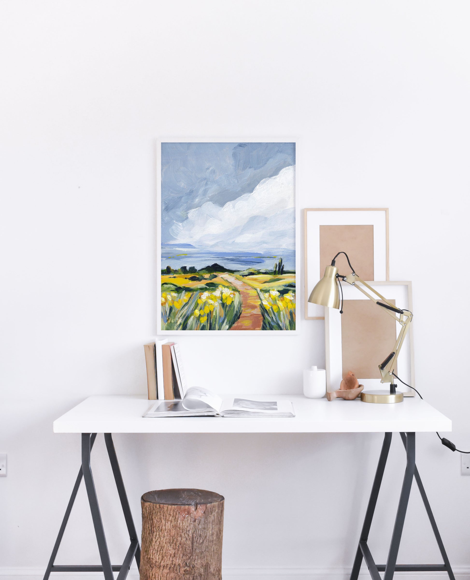 Modern office setup with a desk, lamp, and framed artwork on a white wall.