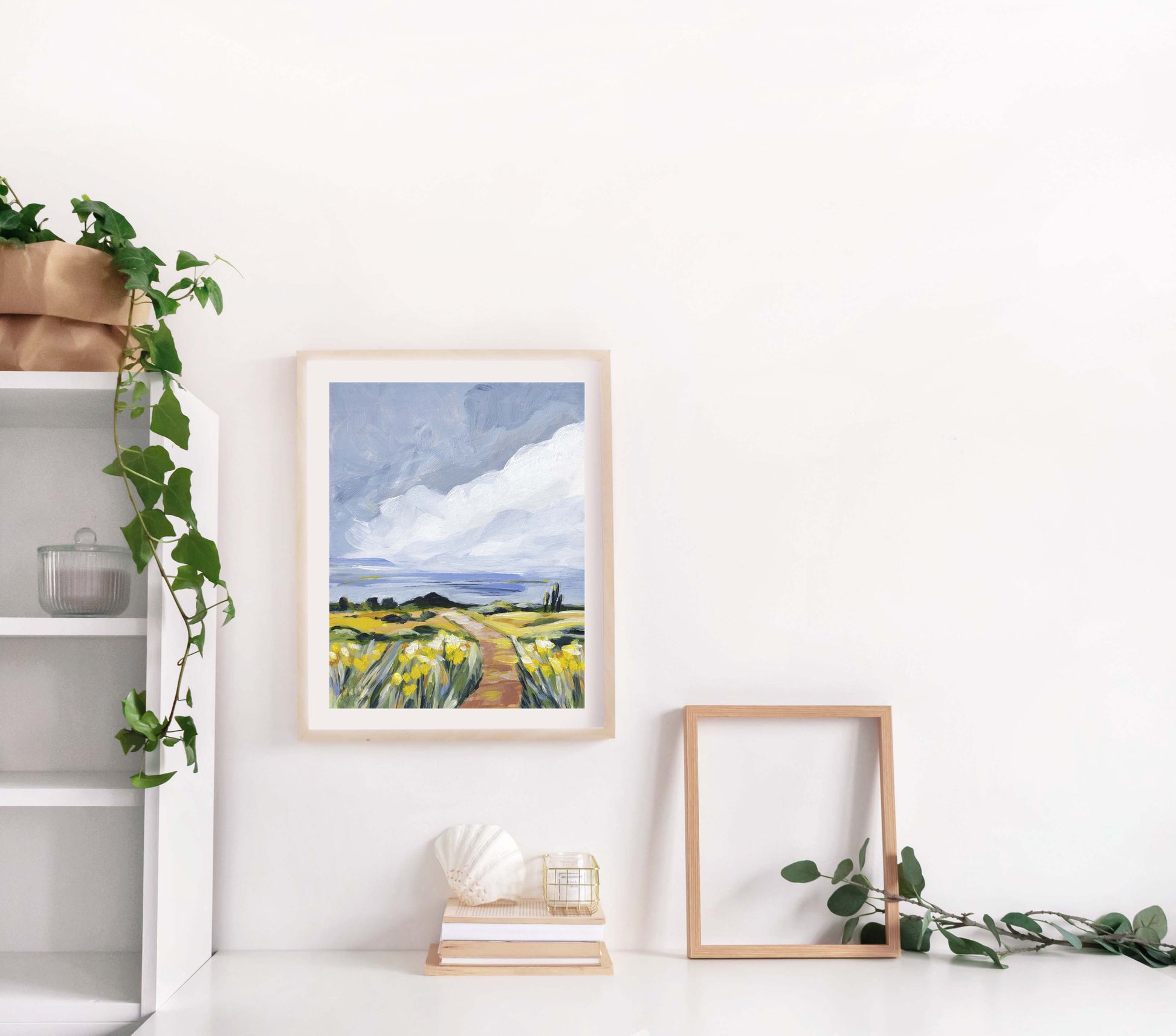 Framed artwork of a landscape with a field and sky, placed on a shelf with decorative items.