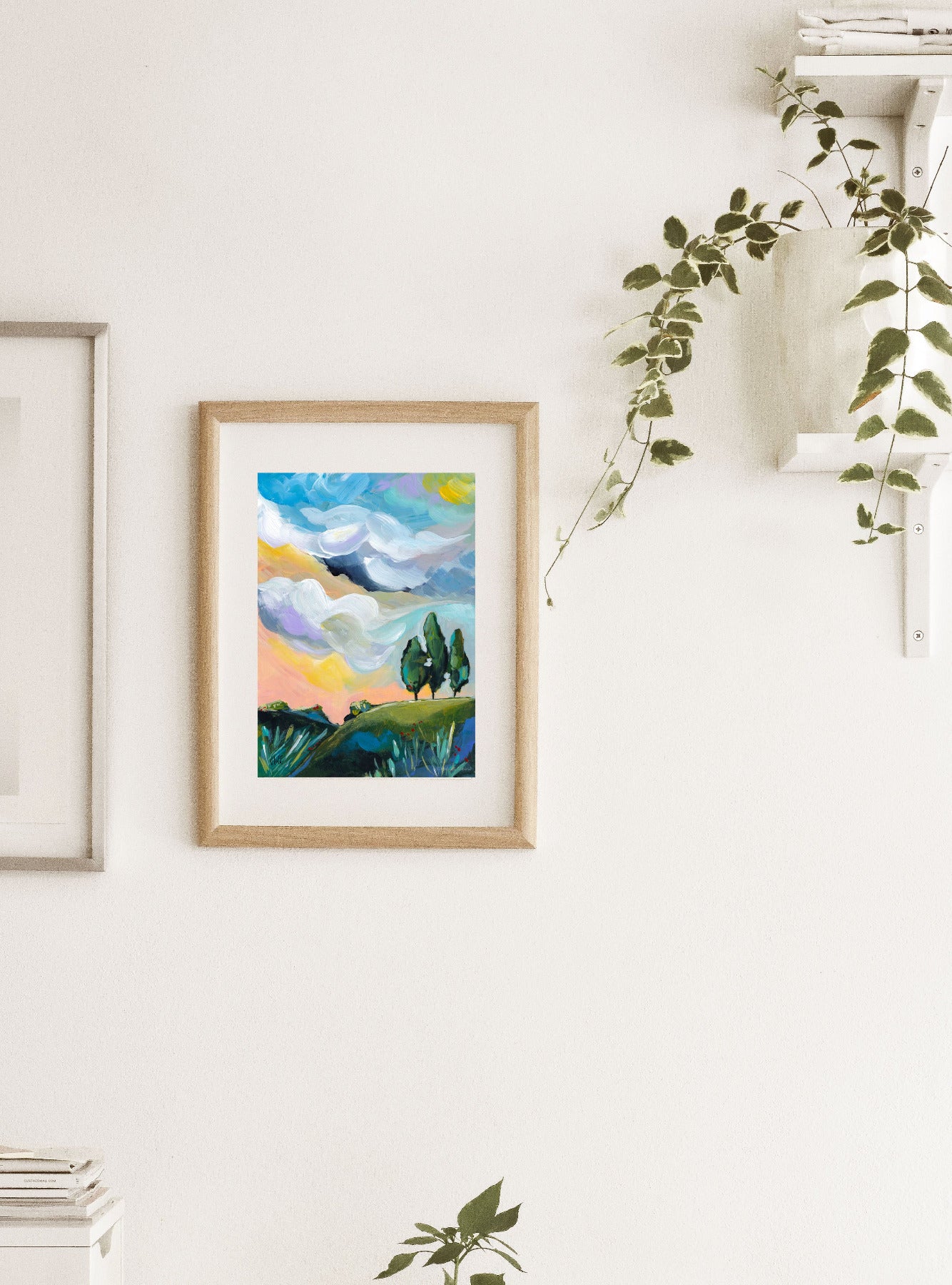 Framed abstract landscape art on a white wall with plants.
