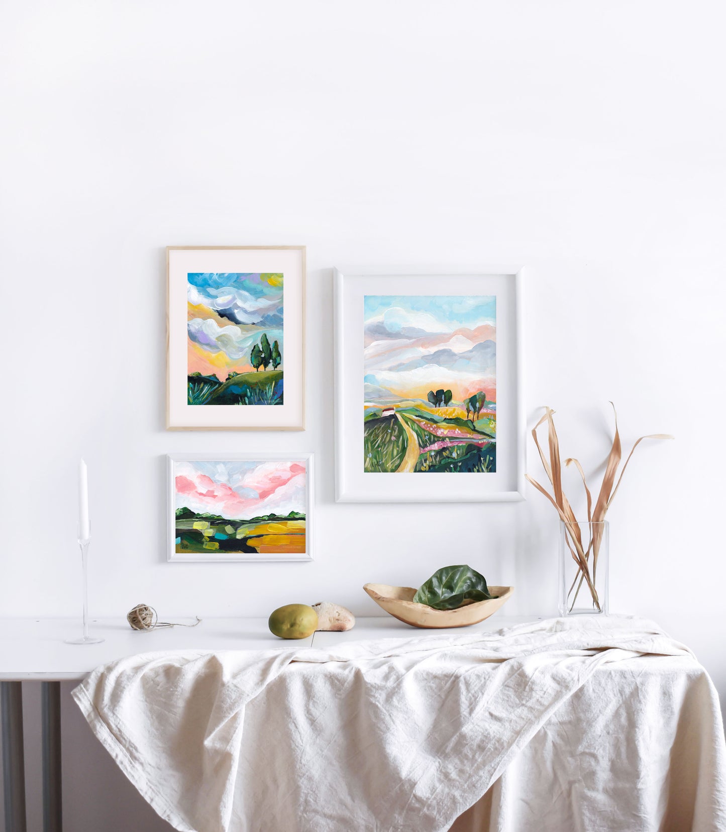 Four framed landscape paintings on a wall above a table with a white tablecloth.