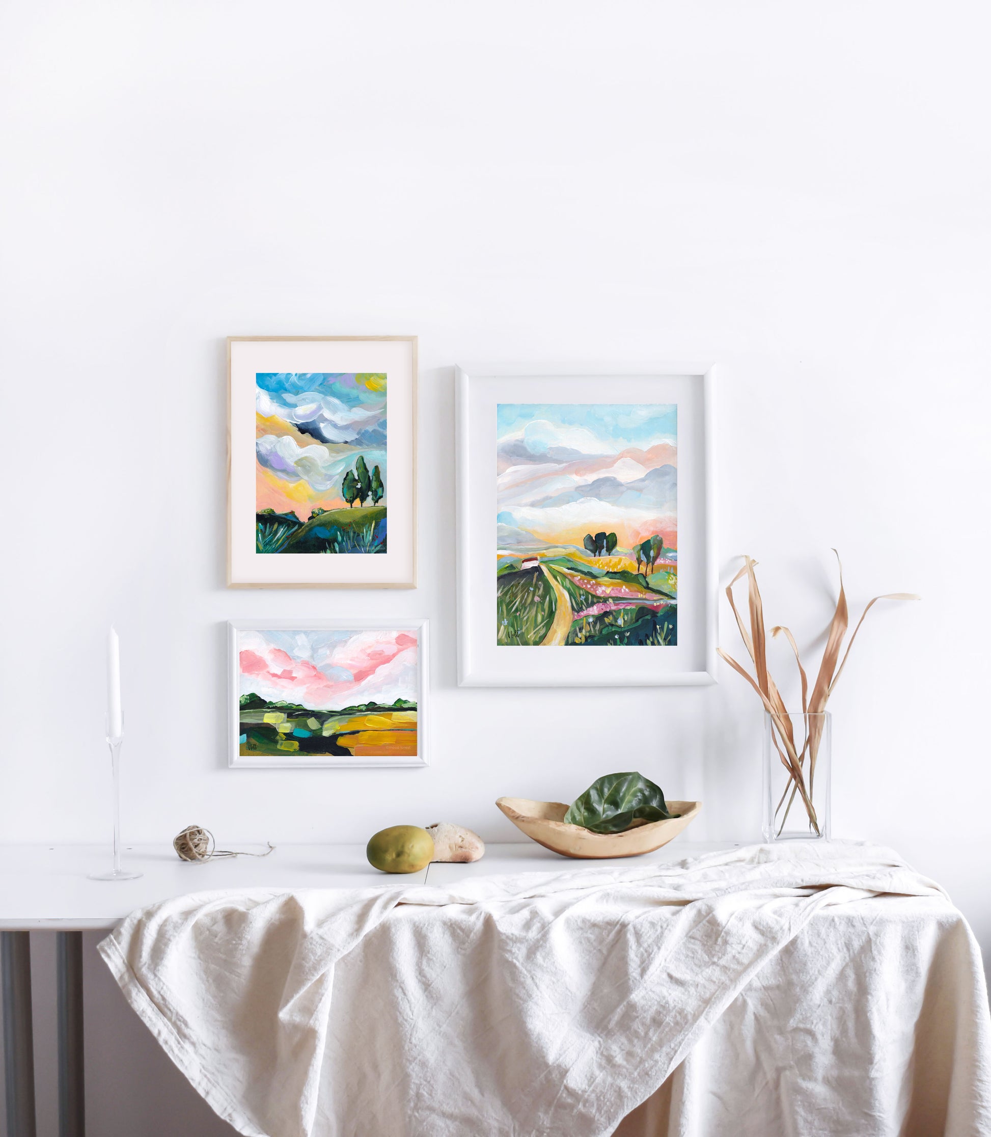 Four framed landscape paintings on a wall above a table with a white tablecloth.