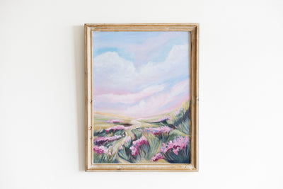 Framed painting of a landscape with pink flowers and mountains on a white wall.