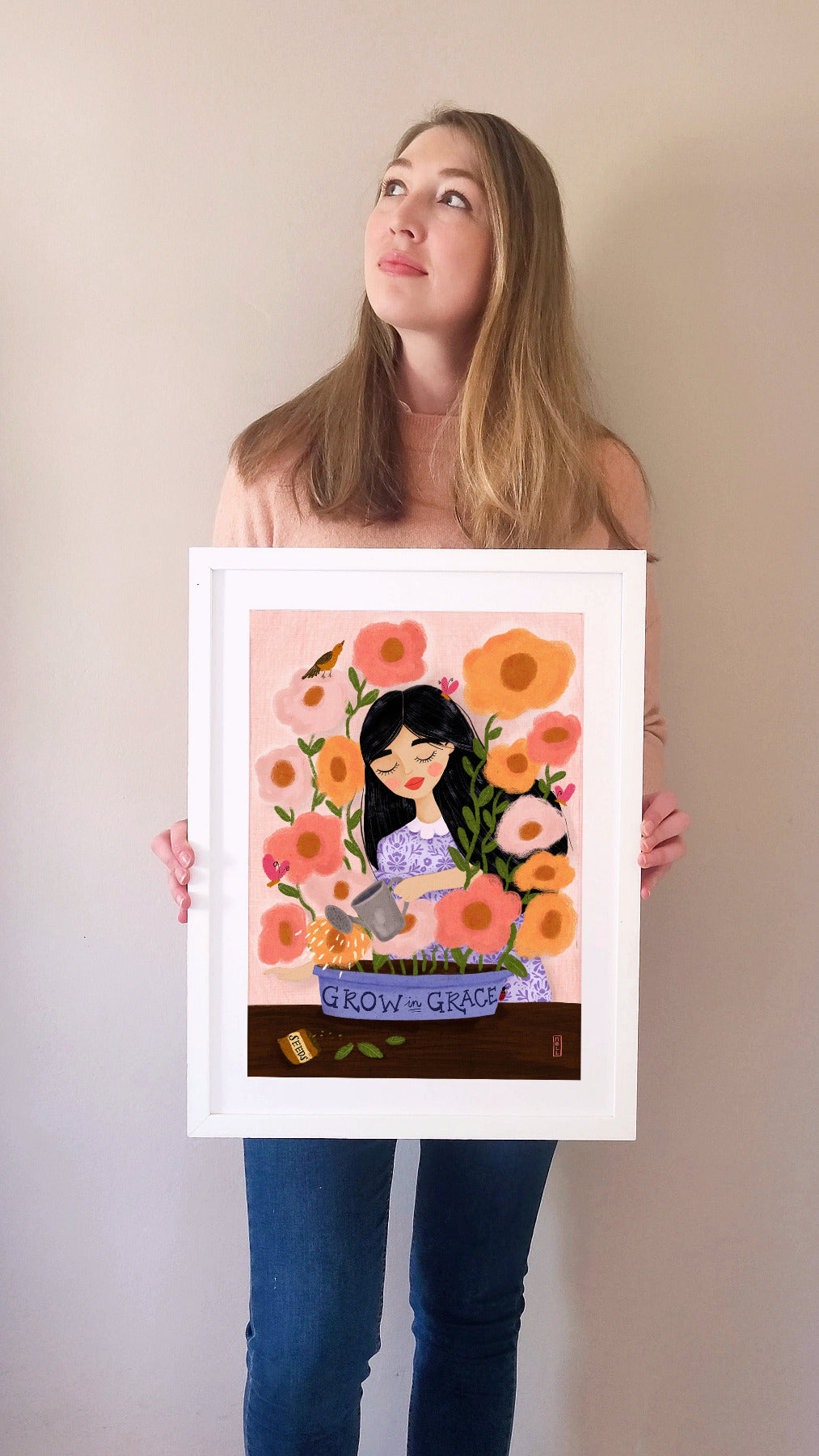 Woman holding a framed illustration of a woman with flowers and 'Grow in Grace' text.