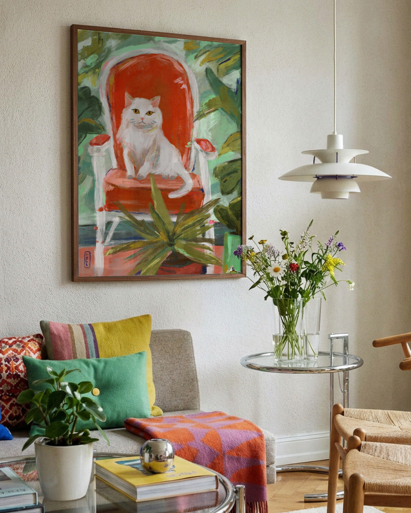 Living room with colorful painting of a cat on a chair, sofa with pillows, and a small table with flowers.