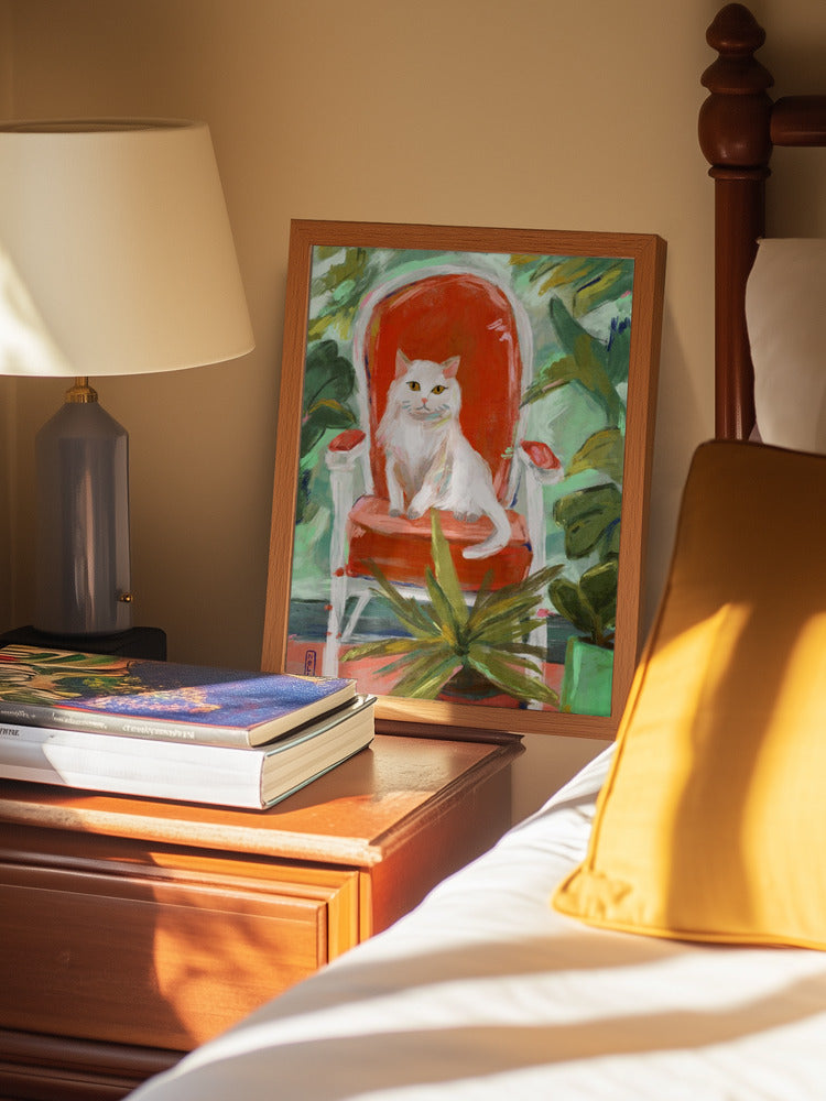 Framed painting of a cat on a chair on a nightstand next to a bed with a yellow pillow.