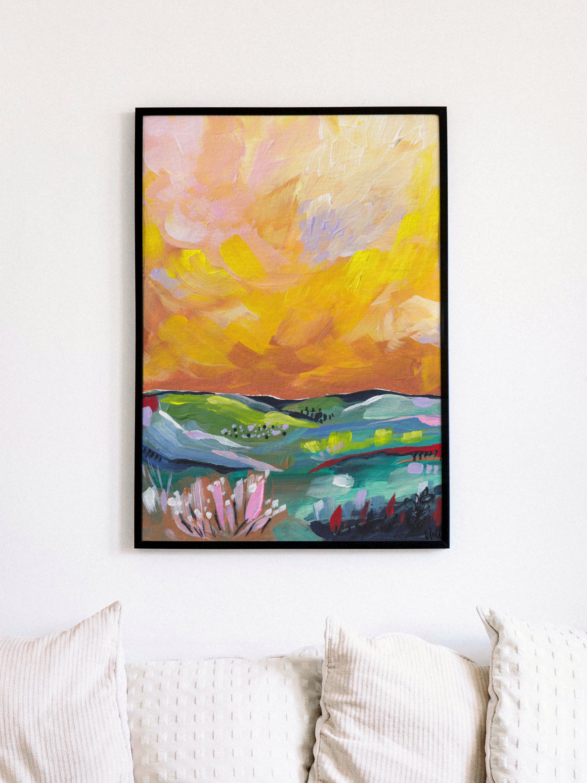 Framed abstract painting with warm colors on a white wall above a sofa.