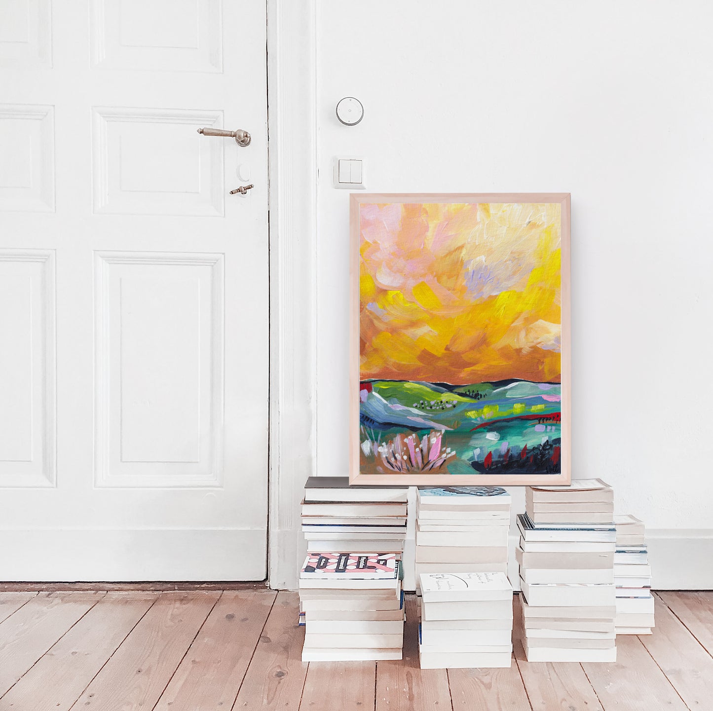 Colorful abstract painting leaning against a white wall with stacks of books below.