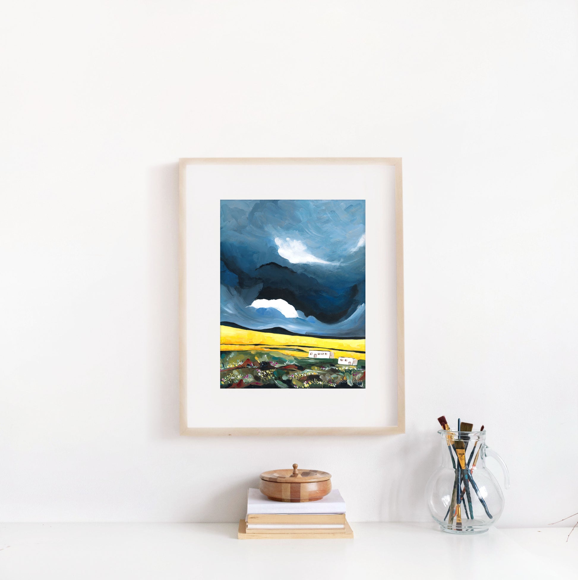 Framed artwork of a landscape with a blue sky and yellow road, displayed on a white wall.