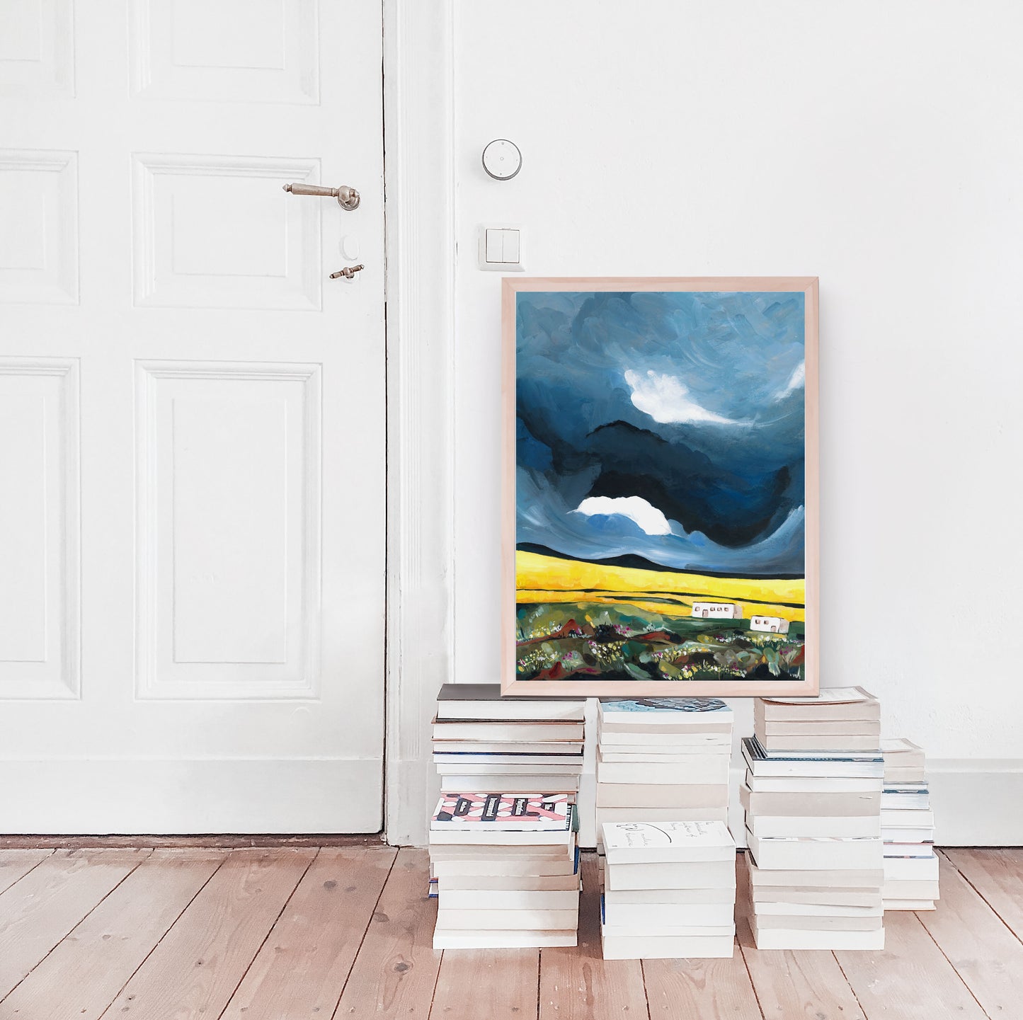 Framed abstract art leaning against a stack of books on a wooden floor.