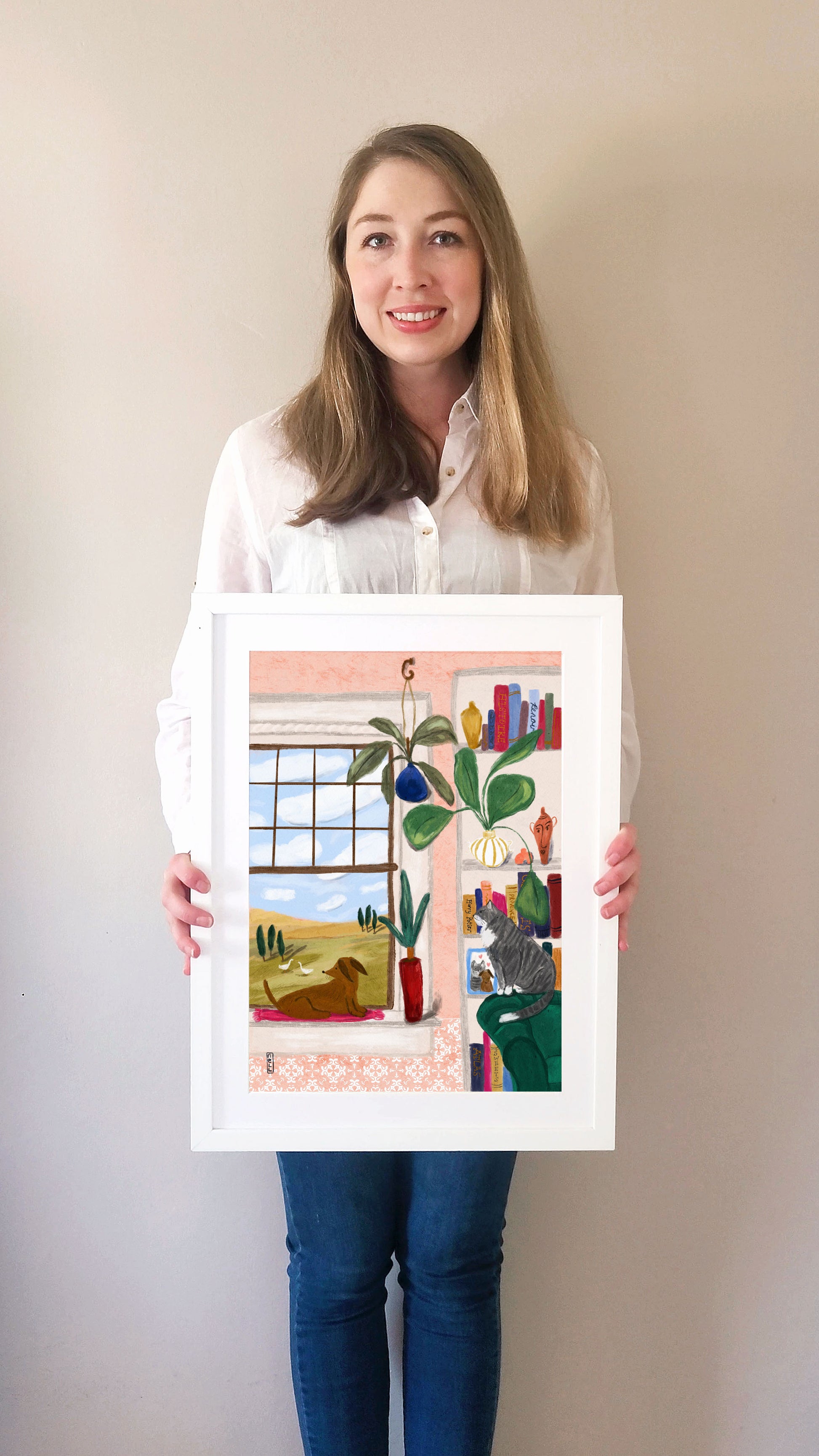 Person holding a framed artwork of a colorful interior scene with plants and books.