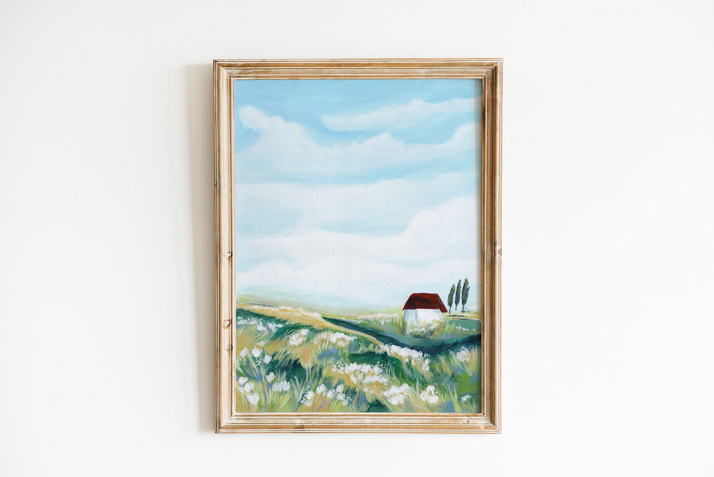Framed painting of a landscape with a house and fields on a white wall