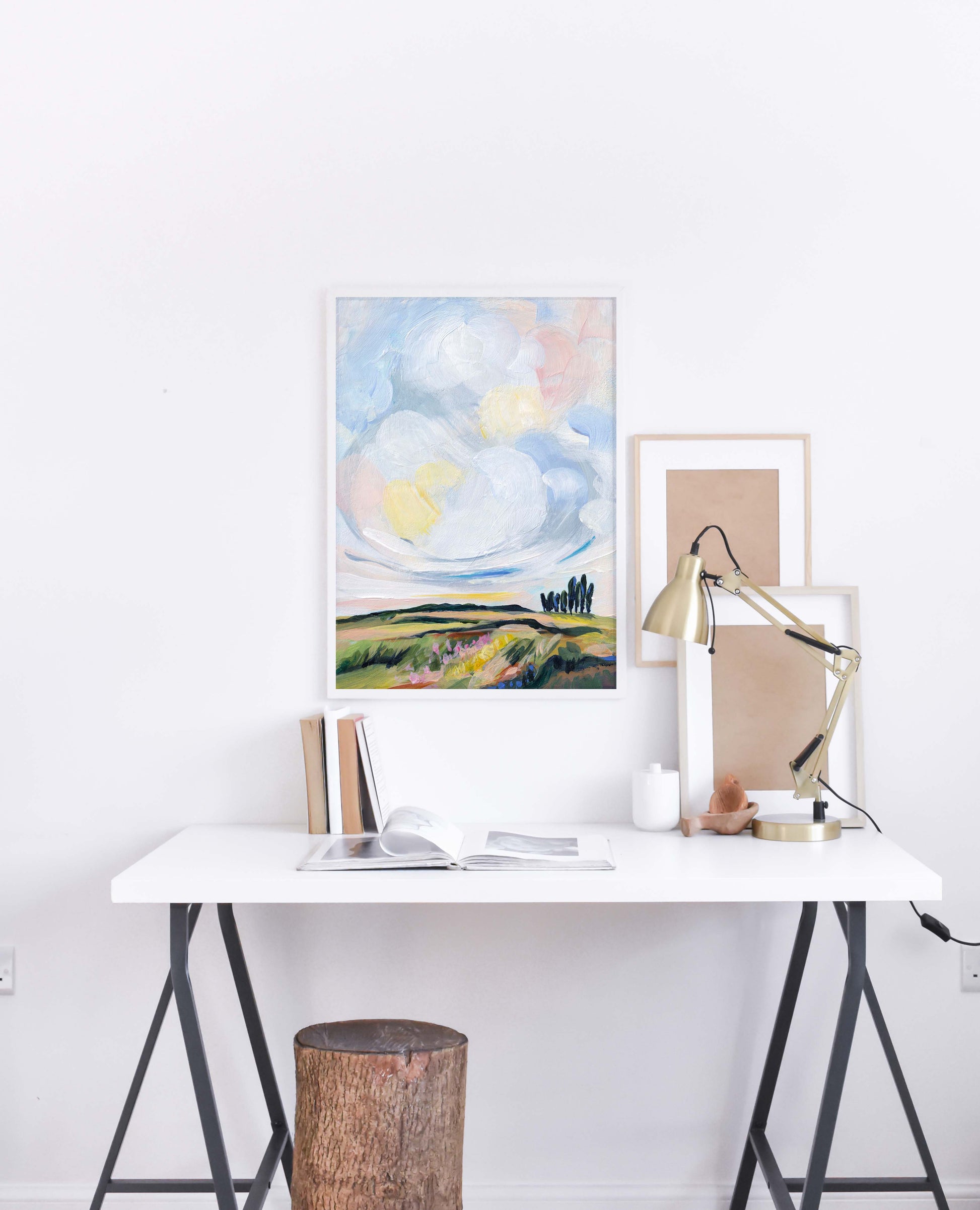 Modern office setup with a desk, lamp, and framed artwork on a white wall.