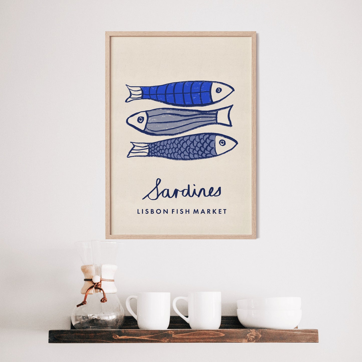 Framed artwork with blue fish illustrations and 'Sardines Lisbon Fish Market' text on a wall above a shelf with mugs.