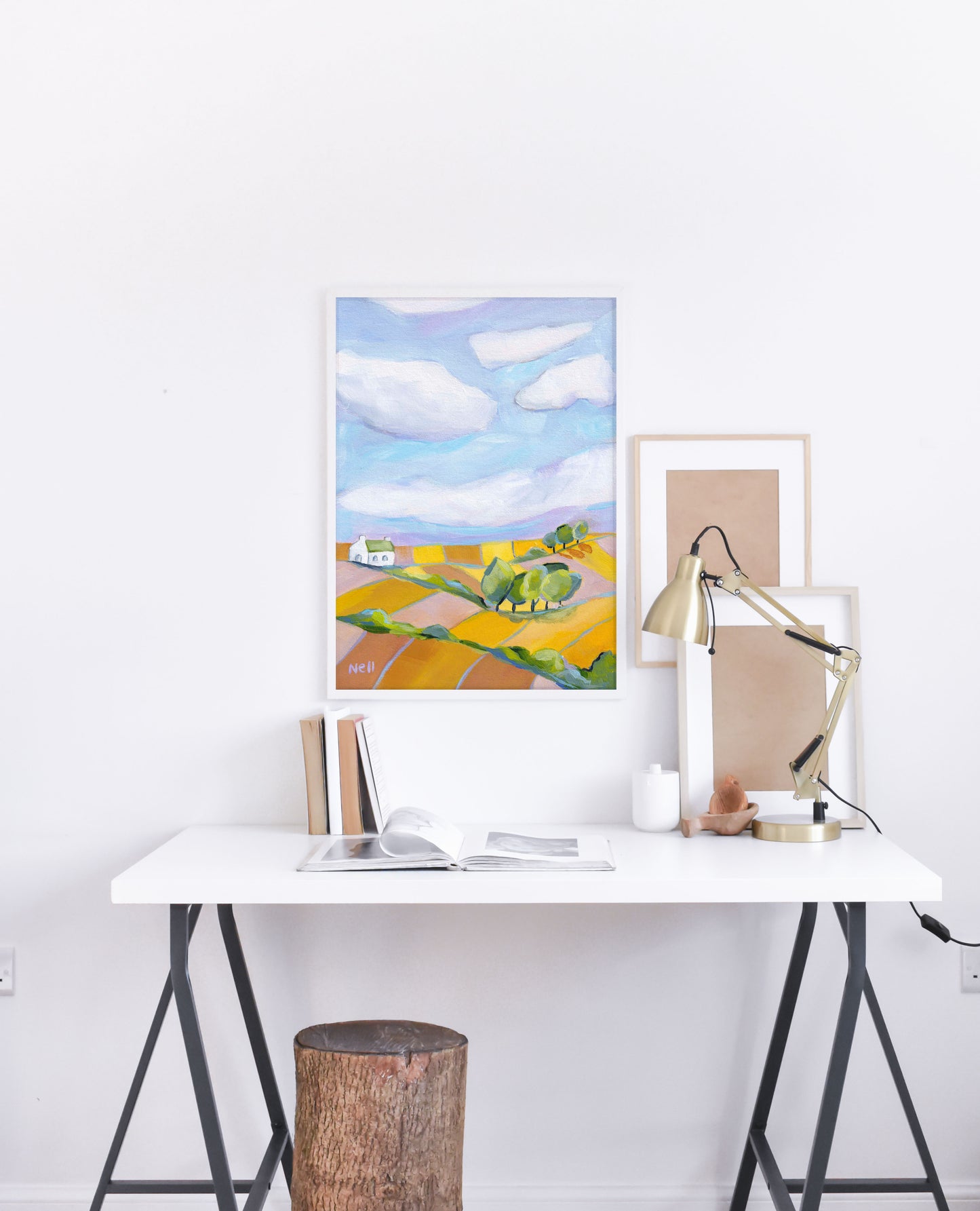 Modern office setup with a desk, lamp, and framed artwork on a white wall.