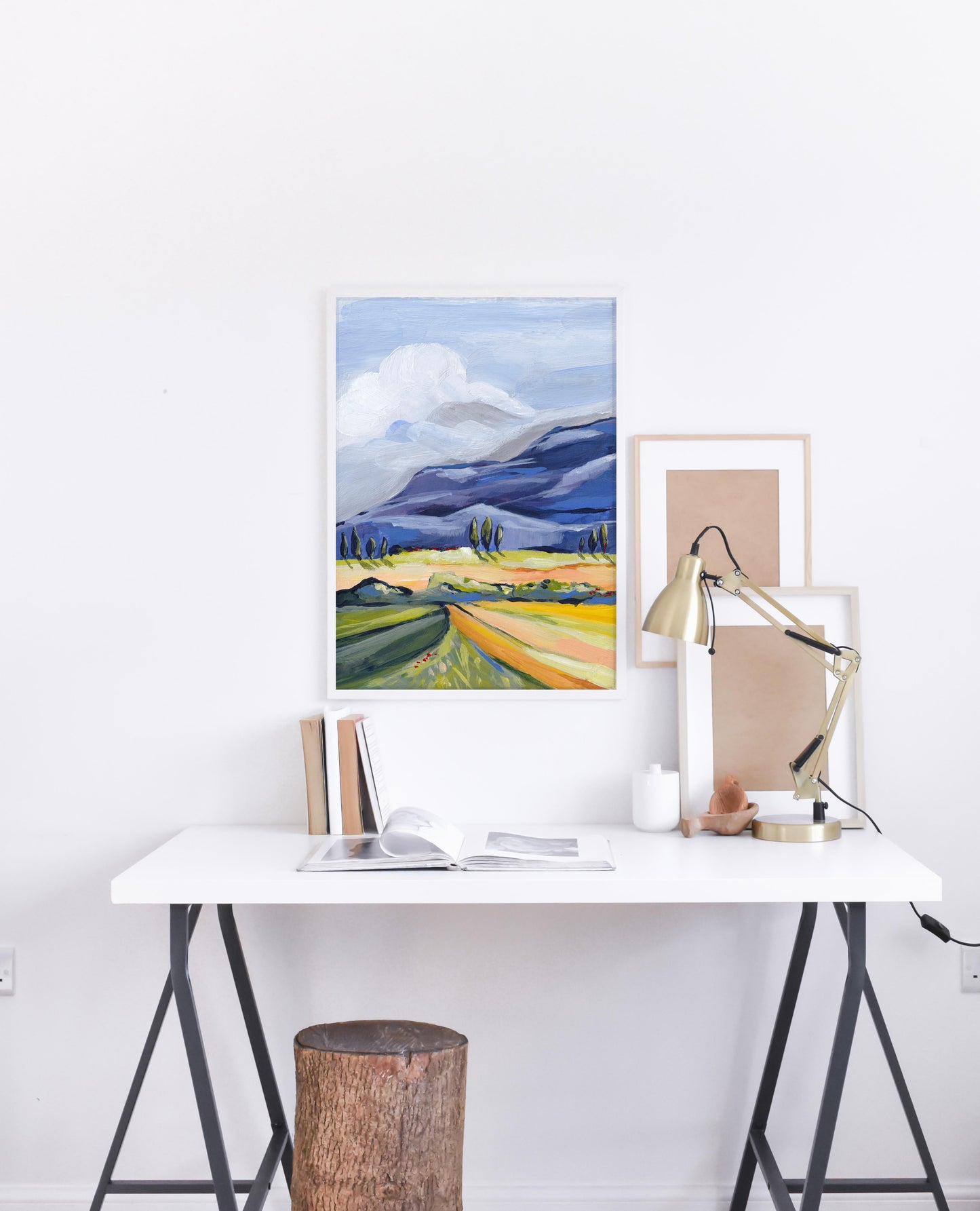 Modern office setup with a desk, lamp, and framed artwork on a white wall.