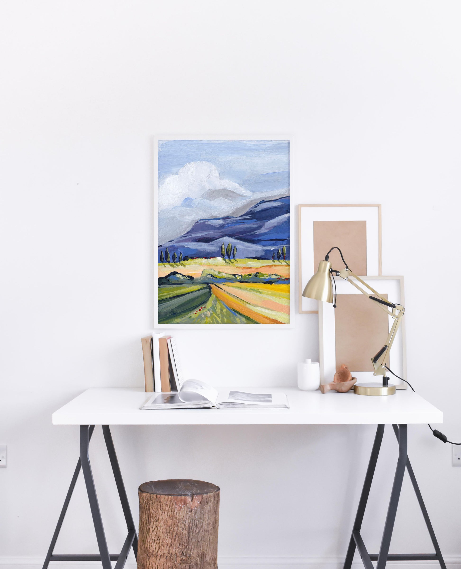 Modern office setup with a desk, lamp, and framed artwork on a white wall.