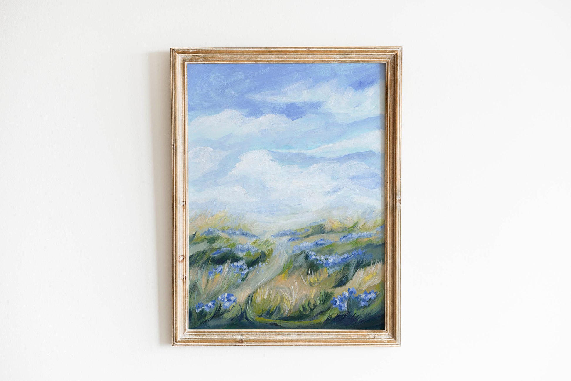 Framed painting of a landscape with blue flowers and a mountain on a white wall
