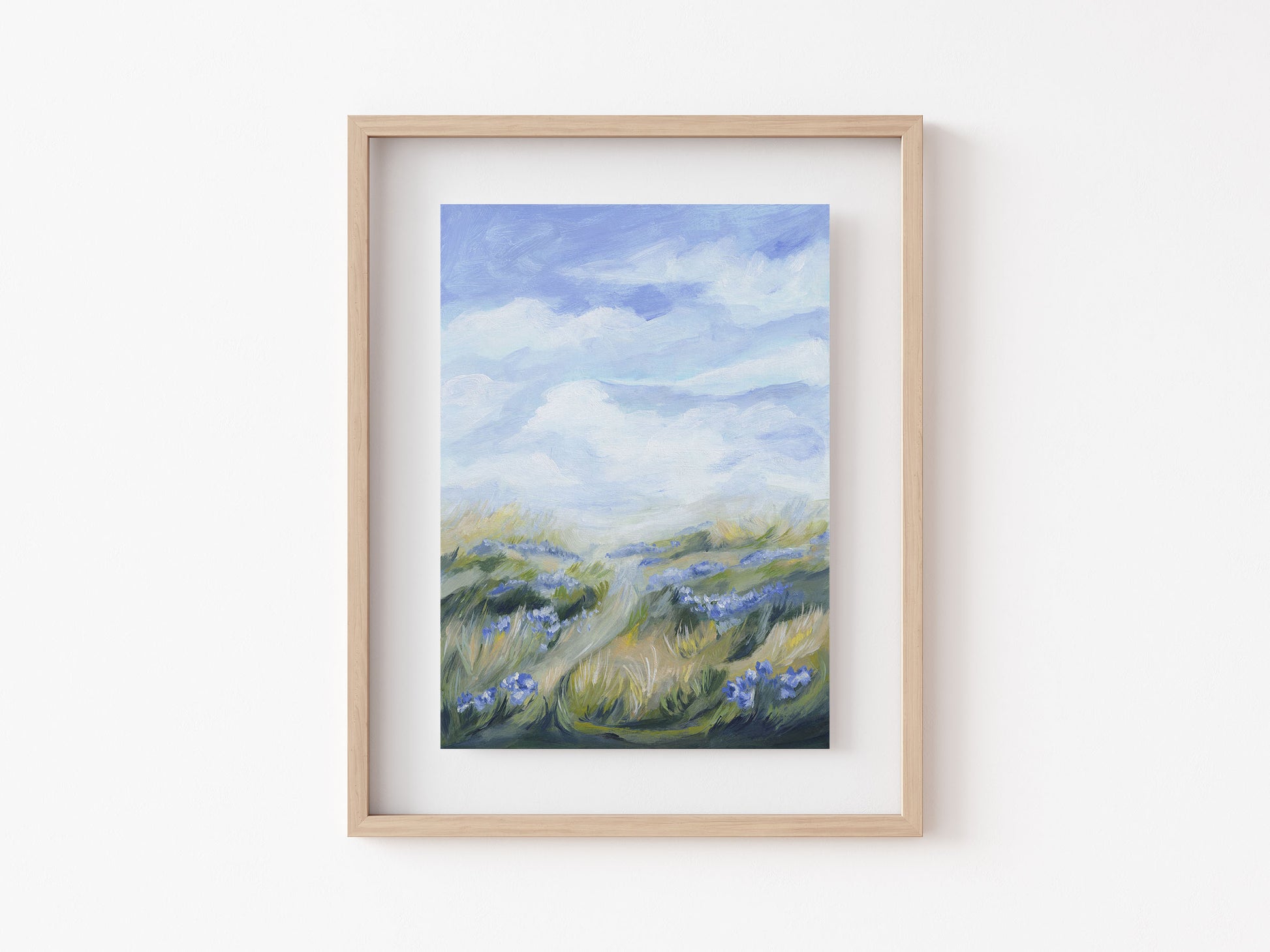 Framed painting of a landscape with grass and clouds on a white wall