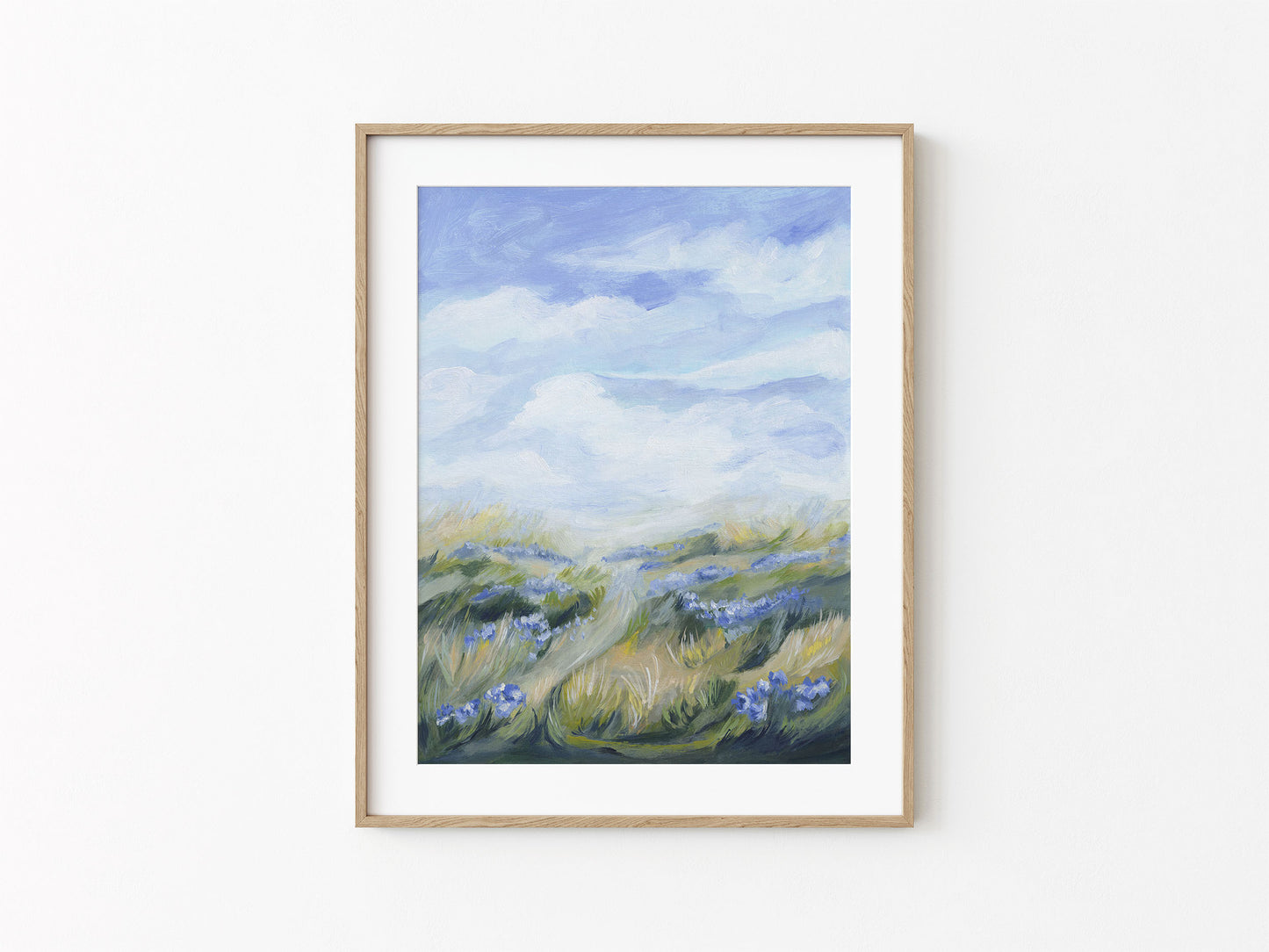 Framed artwork of a landscape with blue sky and green fields on a white wall.