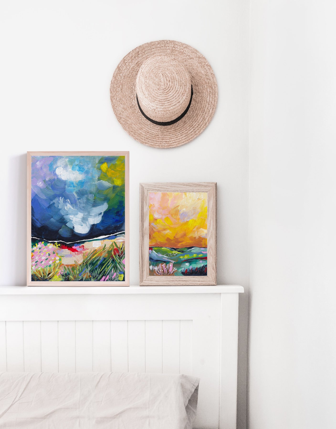 Framed artworks on a white wall with a straw hat above them.