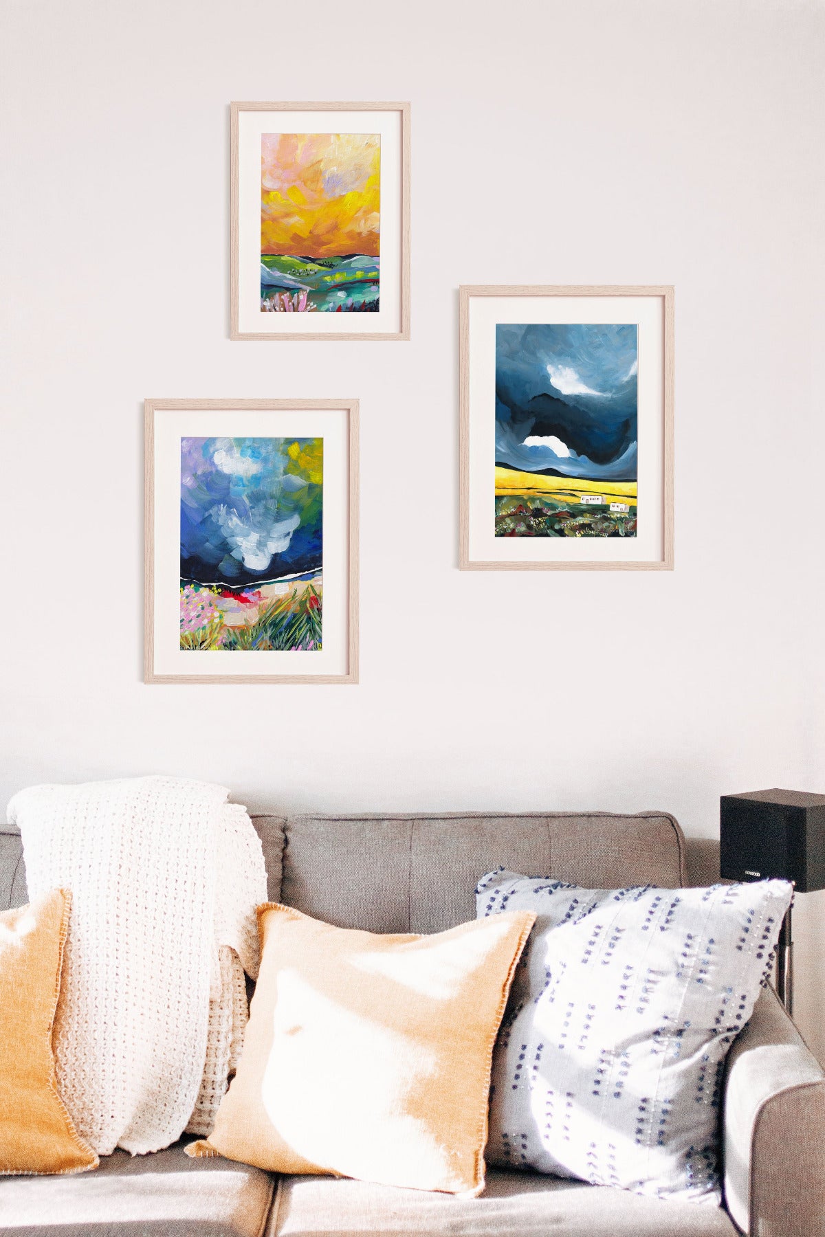 Three framed artworks on a wall above a sofa with colorful cushions.