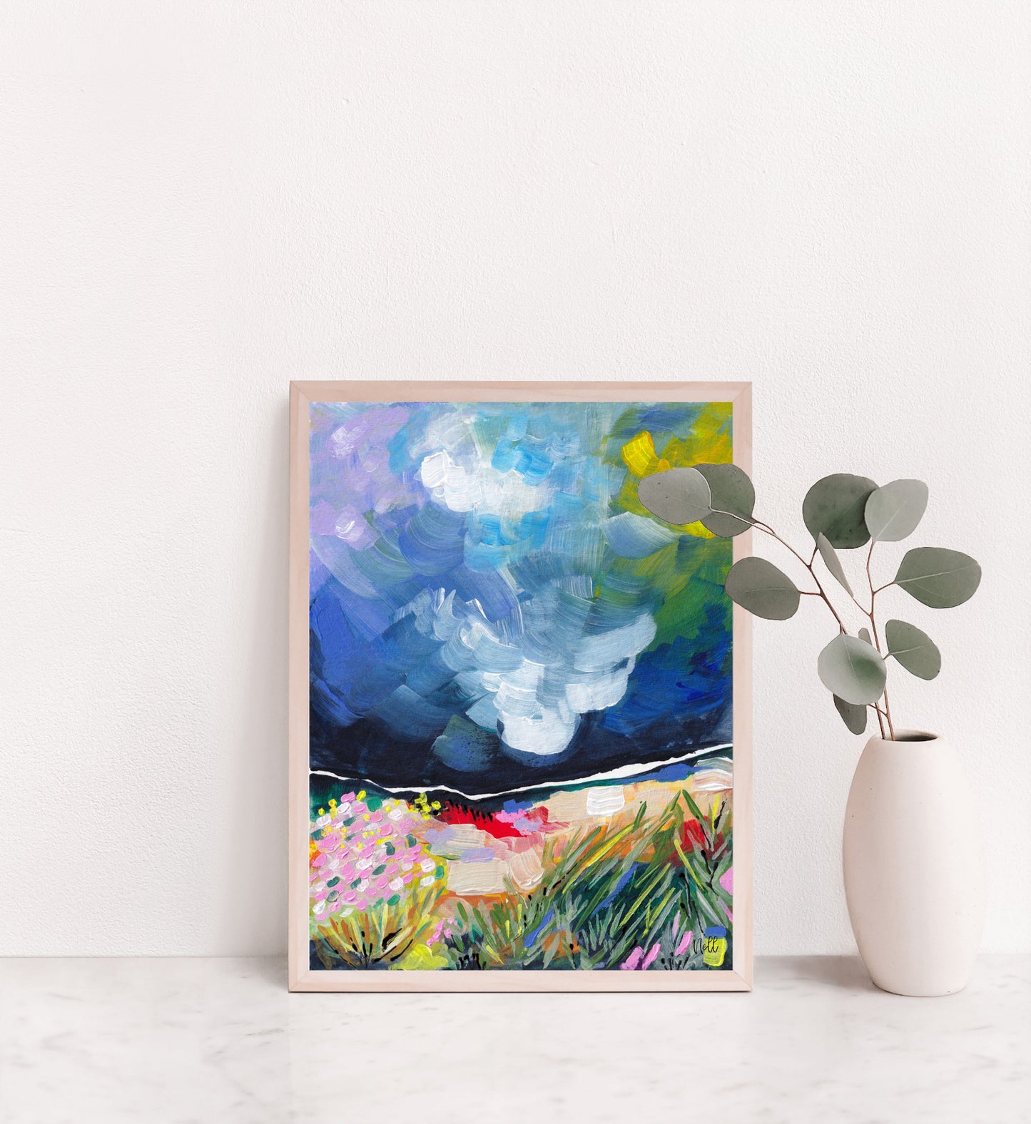 Framed abstract painting on a white wall with a vase of eucalyptus.