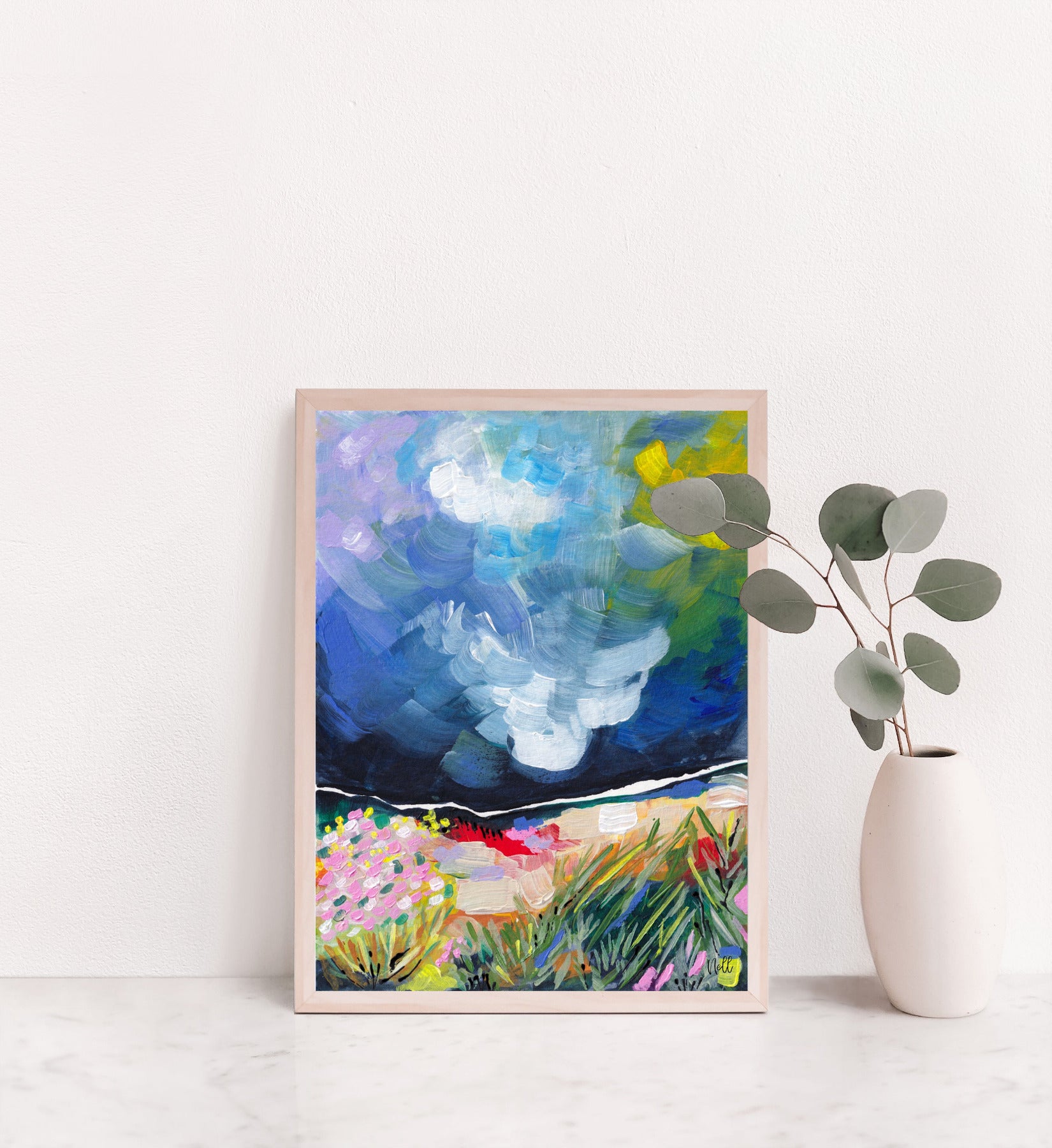 Framed abstract painting on a white wall with a vase of eucalyptus.