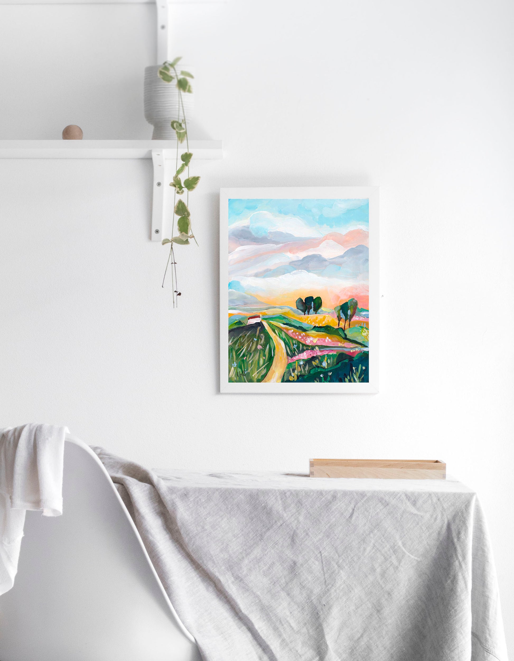 Framed artwork of a landscape with mountains and trees on a white wall.